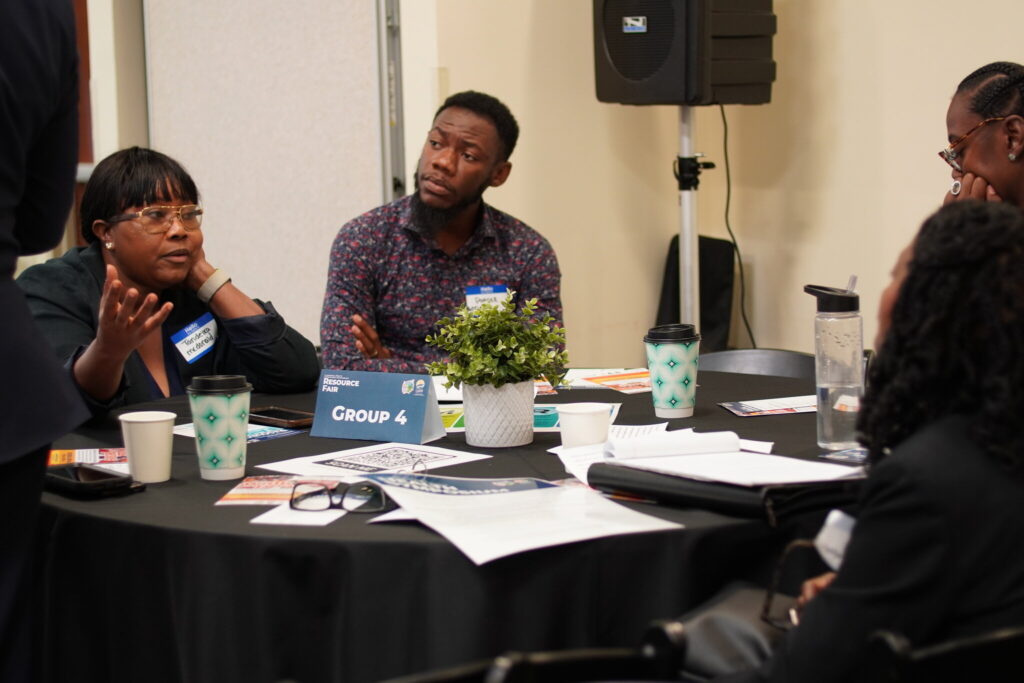 A group of middle aged African American men and women seated at a table in conference.